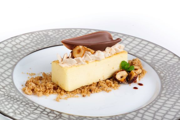 Elegance Milk Schokoladenaufleger in Blattform auf einem Tellerdessert mit American Cheesecake und Crumble drum herum.