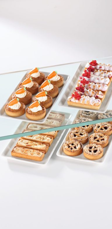 Vitrine mit verschiedenen kleinen Tartelettes in rechteckig und rund, darunter Varianten Carrot Cake und Linzer Tarte.