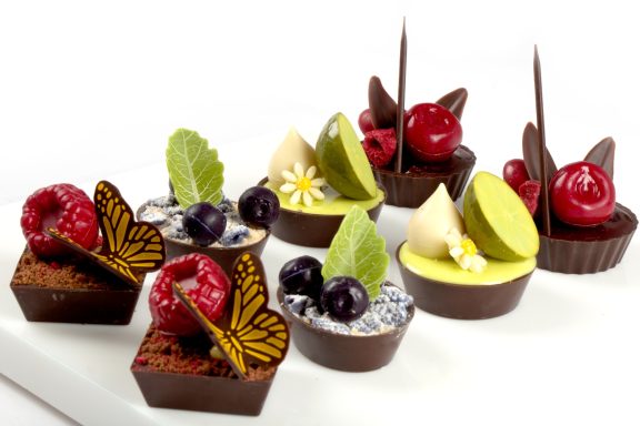 Mehrere Petit Fours Schokoladenschalen gefüllt mit Creme und Obst und dekoriert mit verschiedenen Dobla Schokoladendekoren.