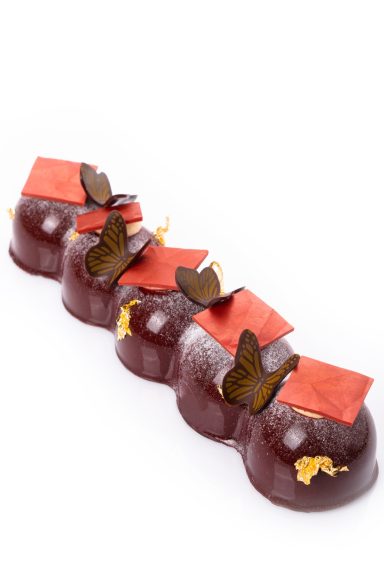 Schmetterlingsdekor und rotes Schokoladendekor in einer Reihe auf Desserts angerichtet.